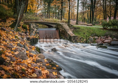 View of autumn river bank with small waterfall. Stones and boulders on river bank. Fast jet of water at slow shutter speeds give a beautiful magic effect. Riga, Latvia.