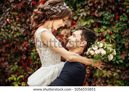 Dark blonde bride looks at groom smiling to her before the wall of ivy