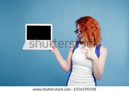beautiful red-haired girl holding a laptop isolate on a blue background. place for text