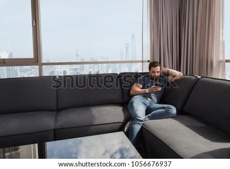 young man sitting on sofa and using a mobile phone  near the window at home