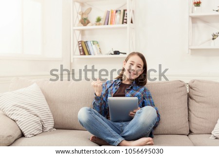 Little girl with digital tablet. Gadgets and technology concept, playing online game, sitting on couch in living room at home, copy space