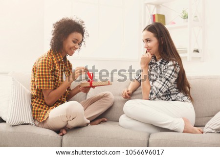 Excited woman getting gift from her girlfriend. Two happy female friends exchanging presents, copy space
