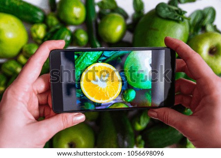 woman take picture on the phone of green fruits with orange in the middle