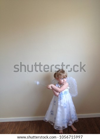 Blond haired girl plays dress up as a white fairy with wand and wings