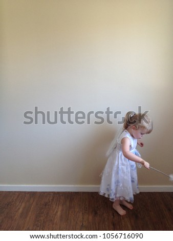 Blond haired girl plays dress up as a white fairy with wand and wings