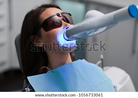 Close-up portrait of a female patient at dentist in the clinic. Teeth whitening procedure with ultraviolet light UV lamp. Royalty-Free Stock Photo #1056733061