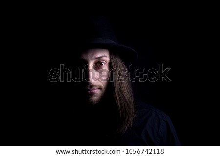 Portrait of mysterious Man with long hair wearing a black hat.Low key isolated photo with free blank space for your text.