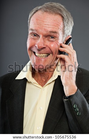 Expressive good looking senior man in dark suit against grey wall. Calling with cell phone. Funny and characteristic. Well dressed. Studio shot.