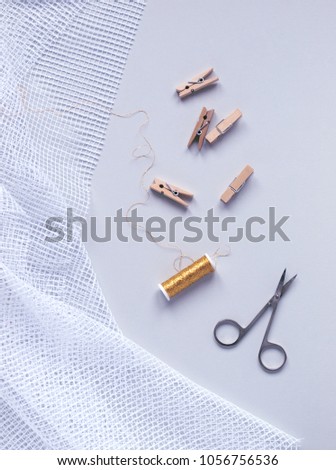 Single gold decorative string next to small wooden clips, scissors and white net fabric on light gray background. Flat lay. Top view