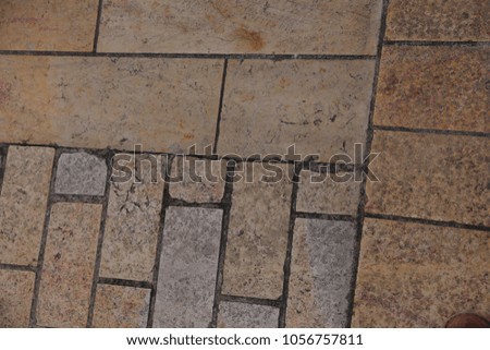 Close up outdoor view of a paved pedestrian walkway. Pattern of rectangular stone elements and dark lines. Beige and grey colours. Abstract urban image. Various rectangles sizes. Ancient city street.