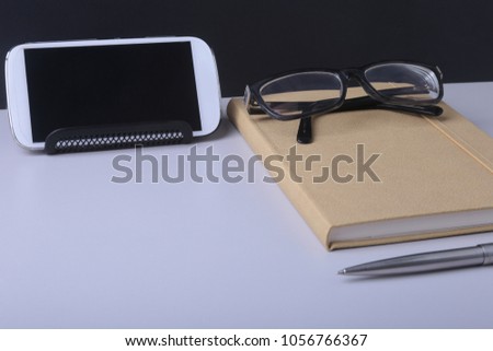 Modern white office desk table with laptop, smartphone and other supplies. Blank notebook page for input the text in the middle. Top view.