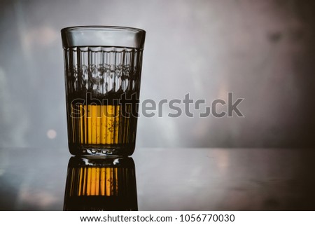 A faceted glass with a dark / light beer on a light blue background with reflection. A faceted glass with a dark / light beer, on a black background with a blue light. vintage photo processing