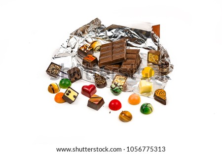 Tile of milk chocolate in a foil wrap and various chocolate candies on a white background
