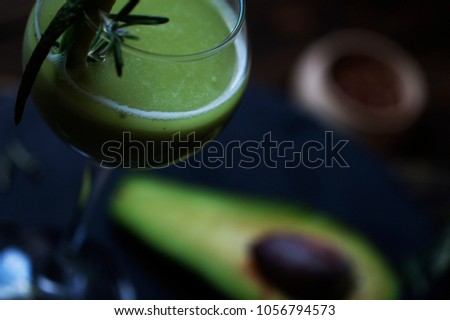Glass of avocado smoothie with drinking straw and mint leaves isolated on white background, top view. Small half piece of avocado. Blur photo studio background. Wooden black table.