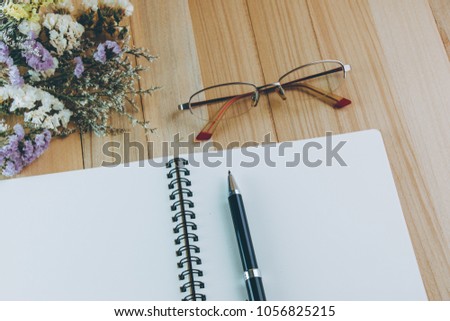 Pen put on blank notebook near bunch of flower blossom, on wooden table