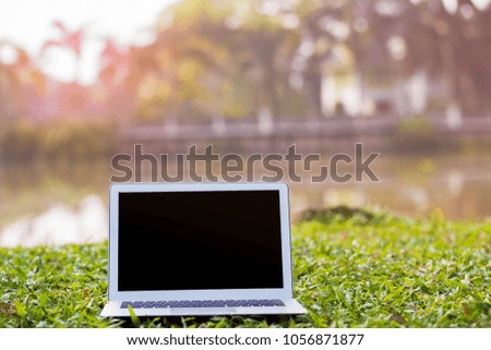 Blank screen laptop on grass blurred nature background.