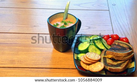 Tomato soup with parsley garnish, fresh vegetables, crackers and a grilled cheese sandwich on an oak table
