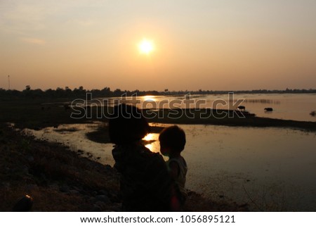 Small children, brothers and sisters standing beside the river at dusk, with golden sun, taking a blurred photo