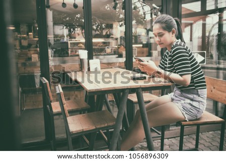 Asian women take a photo with a phone while sitting in a cafe.