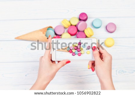 Women's hands holding mobile phone and take pictures of dish from macaroons