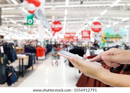 Man use mobile phone, blur image of discounts on department stores as background.