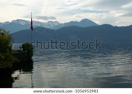 Alpine lake at eveningtime. Cloudy sky and mountains covered by snow on background. Swiss flag on the left. Watercolored picture.