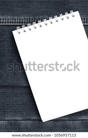 White notebook with clean pages lying on dark blue jeans background. Image with copy space