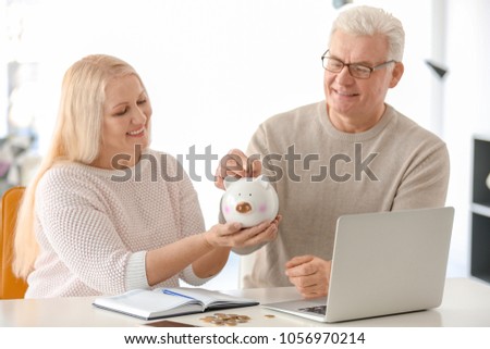 Mature couple putting coin into piggy bank at home. Thinking over pension plan