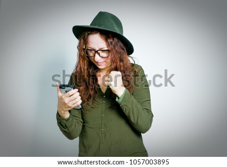 cute red-haired girl looks something online in the phone wearing glasses, isolated on gray background
