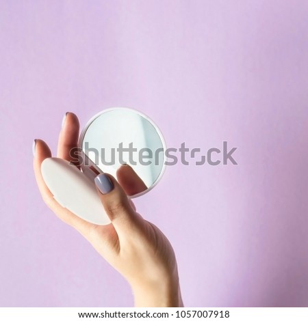 A compact, compact mirror in women's hands. On a lilac bright background. Makeup female accessories Royalty-Free Stock Photo #1057007918