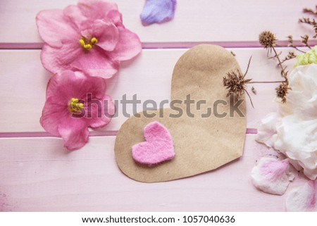 on a pink wooden background lies a card in the shape of a heart for writing, beside lie live colorful flowers