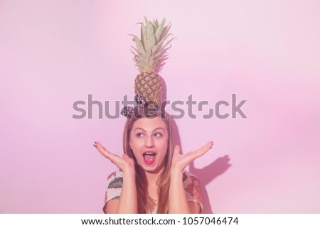Beautiful happy woman holding pineapple on a pink background. Summer concept.