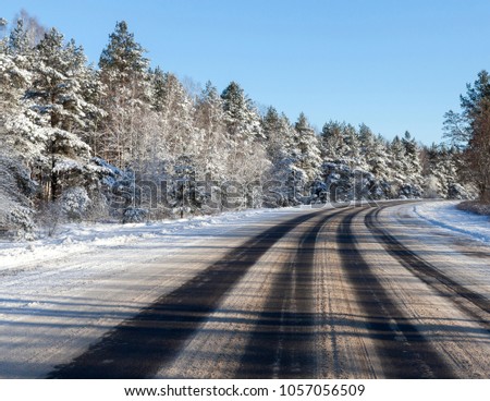picture of the road turning right through the forest in the winter season. Blue sky in the background. Frame made from the center of the roadway