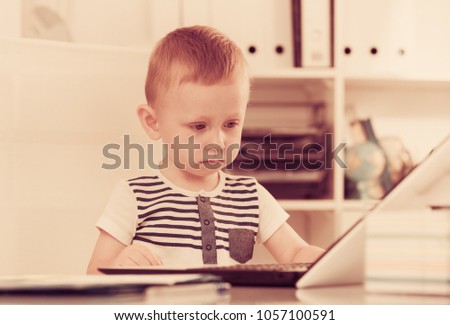 Young cute boy is playing on laptop in the office.