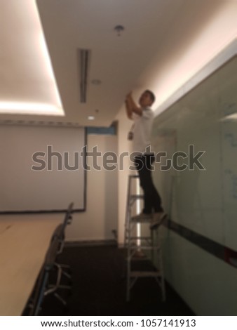 A technician is fixing a light bulb at the ceiling in the meeting room. It's a blurred picture.