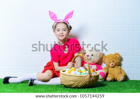 Cute happy little girl wearing bunny ears sits with Easter eggs on a green grass. Kid's fashion. Easter holidays. 