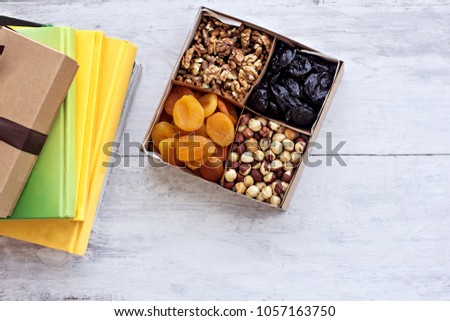 A box of nuts and dried fruits and a stack of books. Dried apricots, prunes, walnuts, hazelnuts.