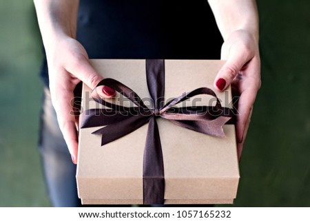 Female hands hold a crafted box with a gift.