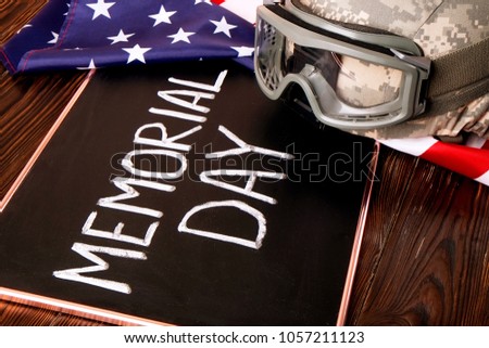 Memorial day weekend text on black chalkboard, USA flag background. US Army kevlar combat helmet camo cover, tactical goggles. Stars & stripes veteran remembrance symbol. Close up, copy space top view