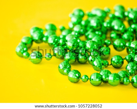 Closeup photograph of a pile of disco ball shaped beads from a plastic green necklace laying on a bright saturated yellow background creating a beautiful juxtaposed colorful background image.