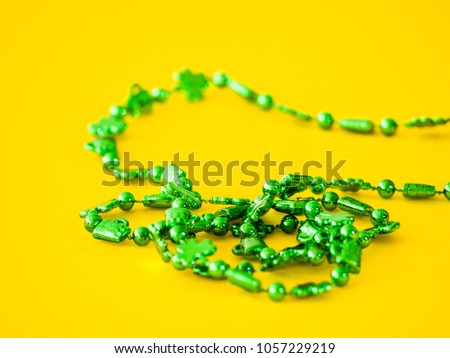 Closeup photograph of a strand of beads from a st. patricks day plastic green necklace with clovers on a bright saturated yellow background creating a beautiful juxtaposed colorful background image.