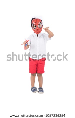 A little kid doing the spiderman movement with his hand and holding a little toy for spider man character and putting his mask, isolated on a white background.