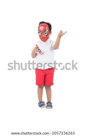 A little kid doing the spiderman movement with his hand and holding a little toy for spider man character and putting his mask, isolated on a white background.