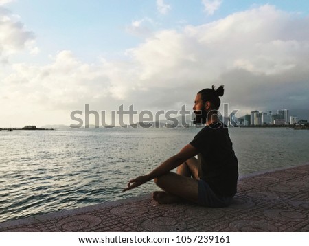 Handsome bearded male sitting in edit action pose by the sea with cityscape in background