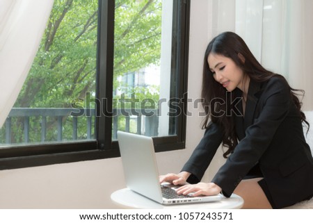 Businesswoman wearing a black suit. Sitting in the room happily.Asian girl wearing black suit is working at notebook computer. -Business Concept