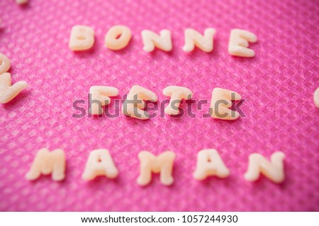 closeup of Pasta forming the text "Bonne Fete Maman" - meaning "Happy Mothers Day" in French in pink background 