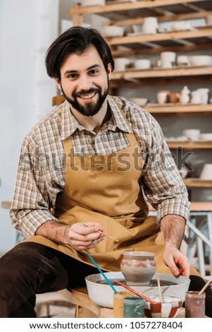 smiling male potter painting ceramic jug in workshop