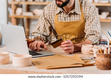 cropped view of potter shopping online with laptop and credit card in workshop