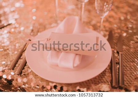 Someone's seat. Plate with white card placed on table with golden sequins tablecloth