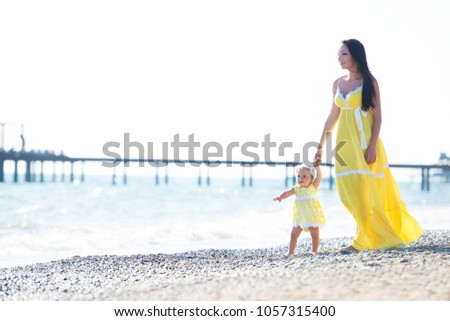 happy family in a yellow dress. Mother and child are walking on the beach